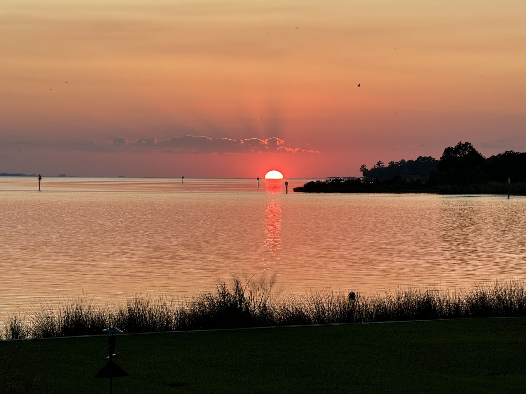 A red setting sun casts a reflection across calm water