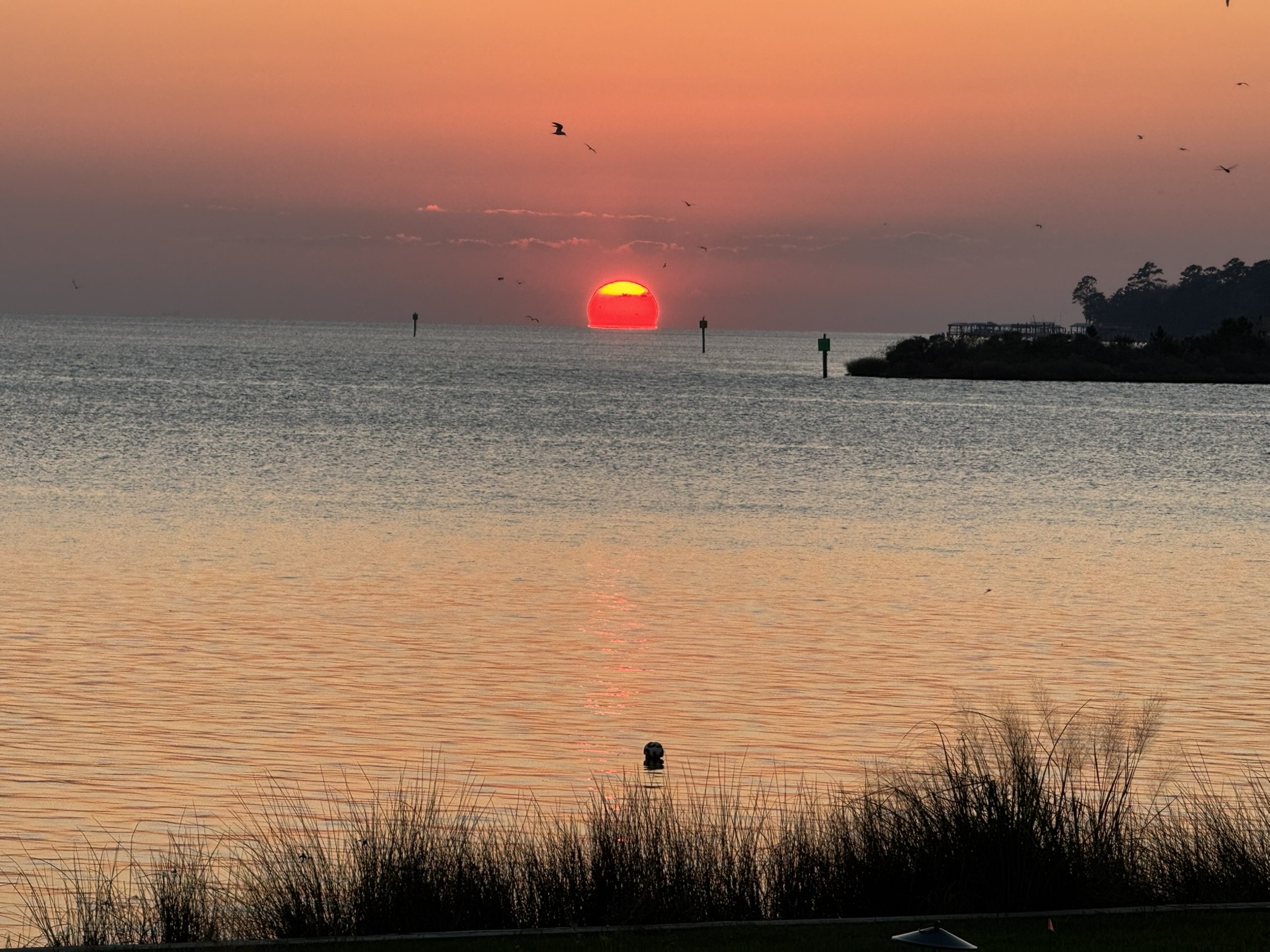 A small red sun sinks toward the water beneath a muted pink sky