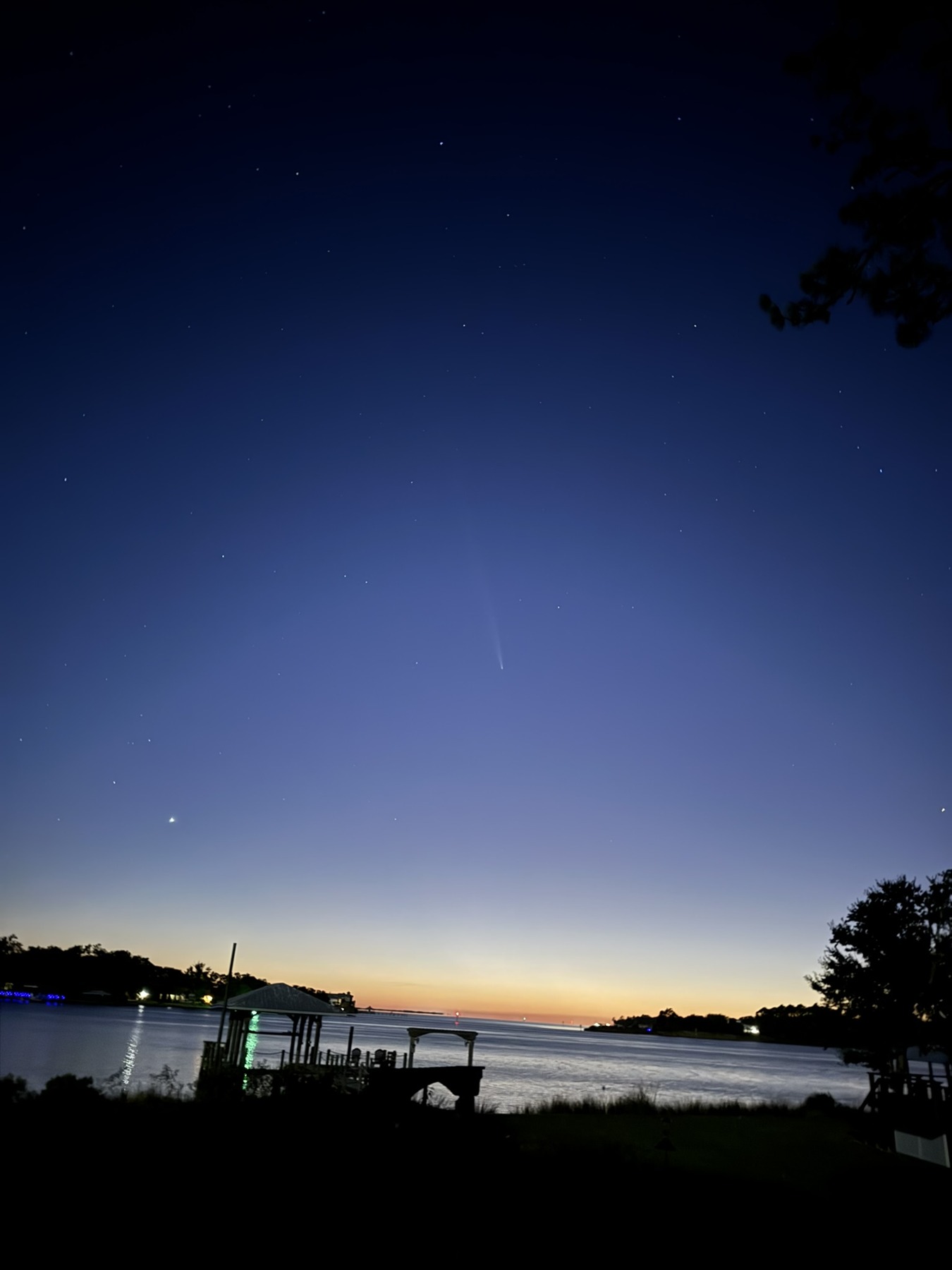 A narrow bright trail in a deep blue twilight sky above the water
